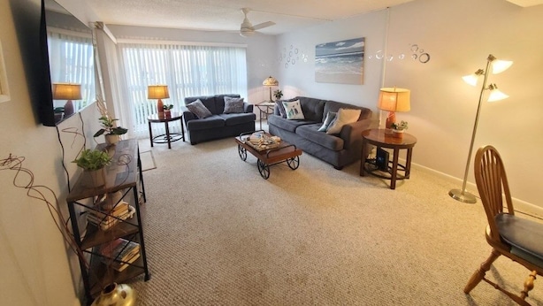 A living room with a sofa, two side tables, a coffee table, a chair, a TV, and a ceiling fan. - Tradewinds 151 1 Bedroom Condo (St. Augustine)