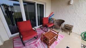 A balcony with a red chair, a wicker chair, and a small table. - Tradewinds 151 1 Bedroom Condo (St. Augustine)