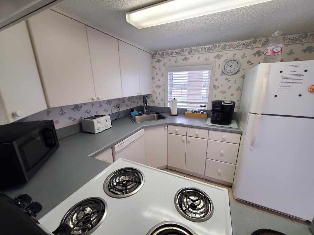 A compact kitchen with a white stove, a microwave, a sink, and a refrigerator.