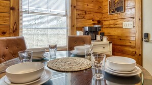 A wooden interior with a dining table set for four, including plates, bowls, and glasses. - Greenbrier Woods 2 Bedroom Cabin (Gatlinburg)