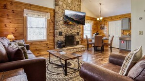 A cozy cabin interior with a stone fireplace, wooden walls, a dining area, and a kitchen. - Greenbrier Woods 2 Bedroom Cabin (Gatlinburg)