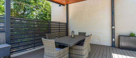 An outdoor patio with a wooden deck, a table with wicker chairs, and a ceiling fan.