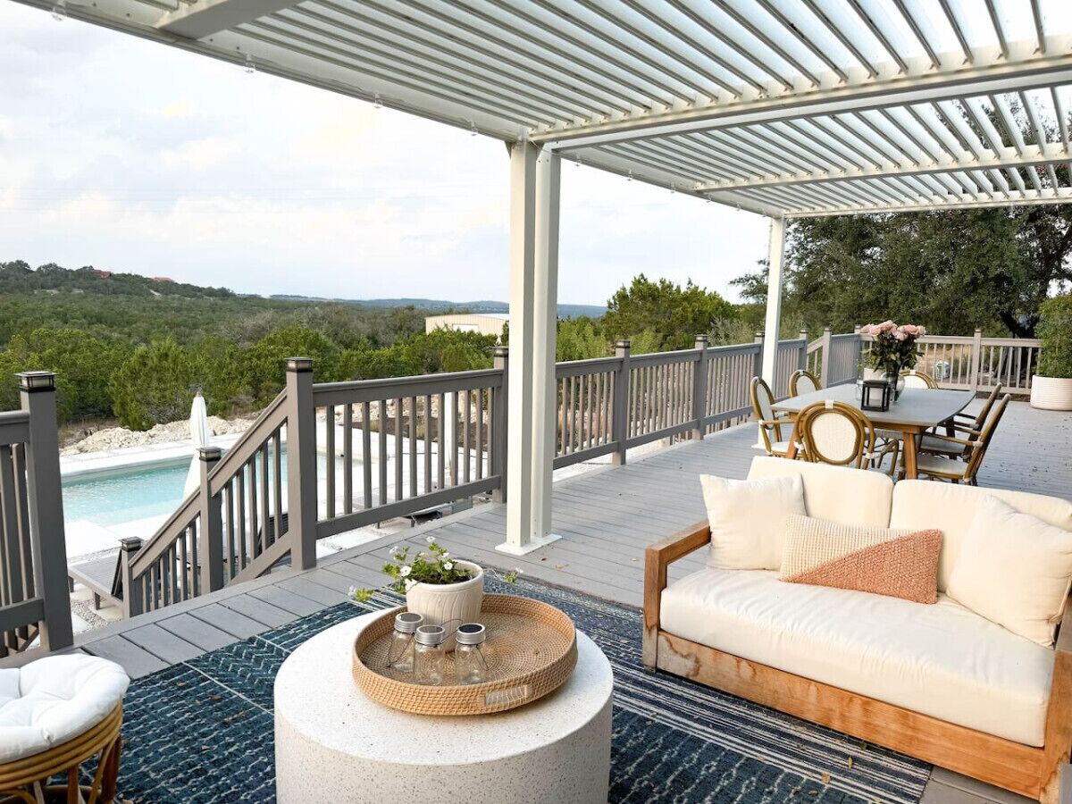A covered outdoor area with a pool, a wooden deck, a white sofa, and a dining table with chairs.