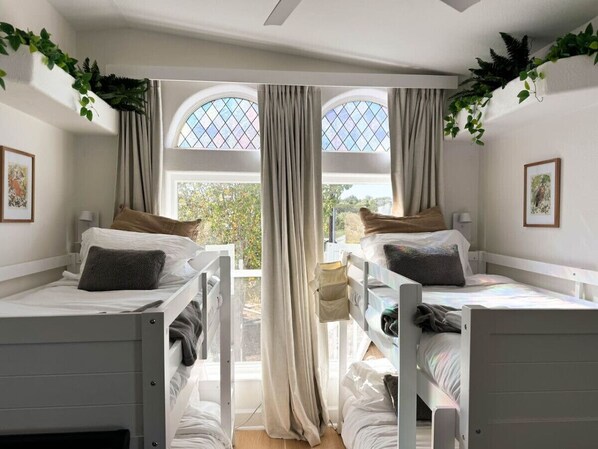 A room with two bunk beds, a large window with curtains, and greenery on the walls.
