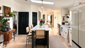 Una cocina moderna con una isla central, sillas de madera, una mesa de comedor y una puerta negra.