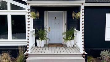 A house with a white door, number 167, a porch with steps, and potted plants on either side.