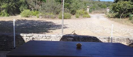 An outdoor table with a stone wall and a view of a dirt path leading through a wooded area.