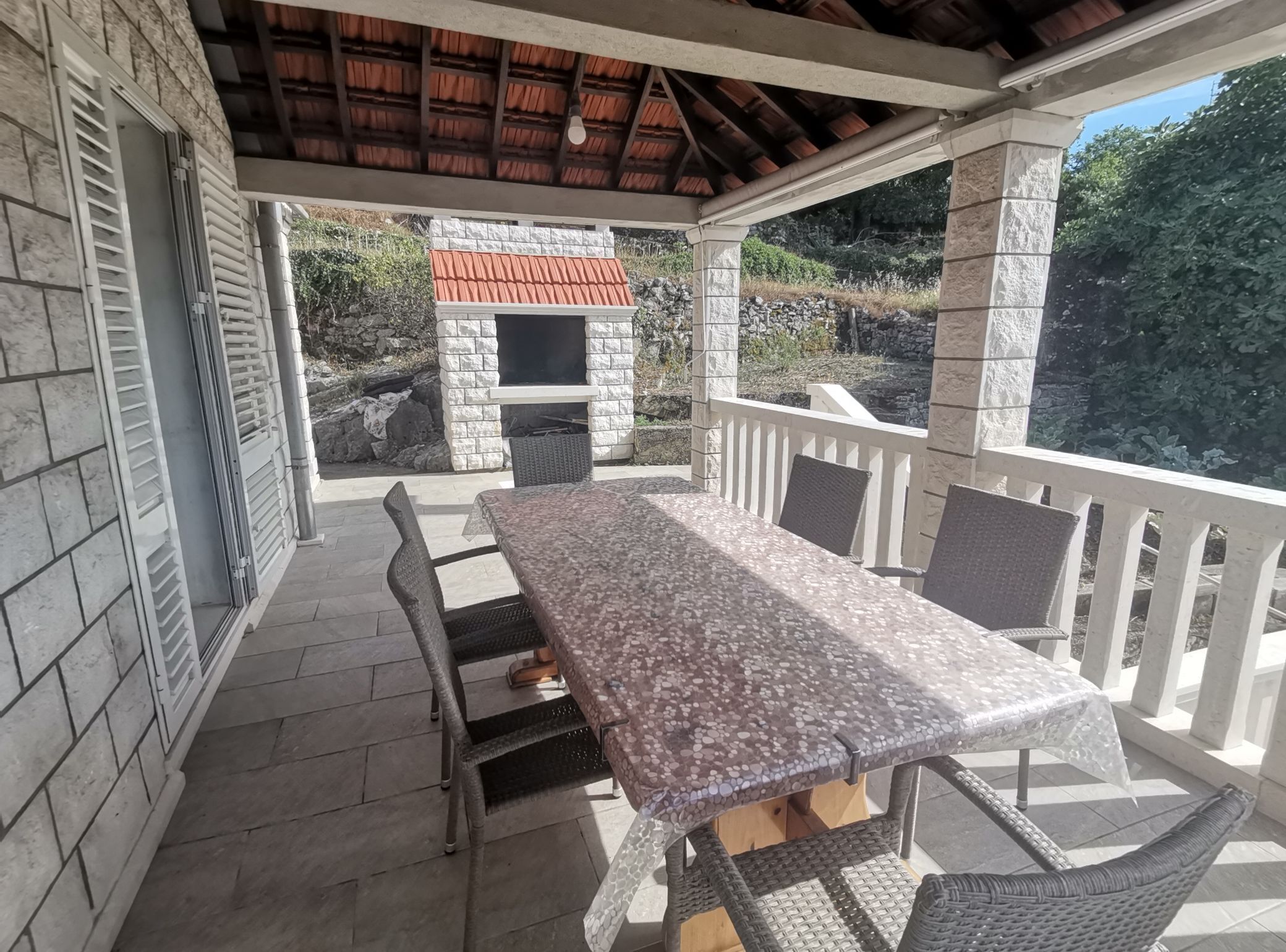 A covered patio with a stone wall, a grill, and a table with chairs.