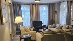 Ein Wohnzimmer mit einer Couch, Sesseln, einem Couchtisch, einem Fernseher und einem Ventilator.