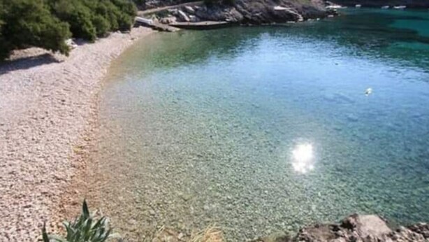 A coastal landscape with a pebble beach and clear turquoise water.