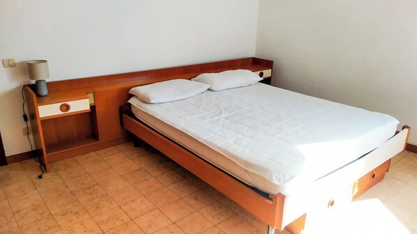 Un lit simple avec une tête de lit en bois, une table de chevet avec une lampe et une commode.