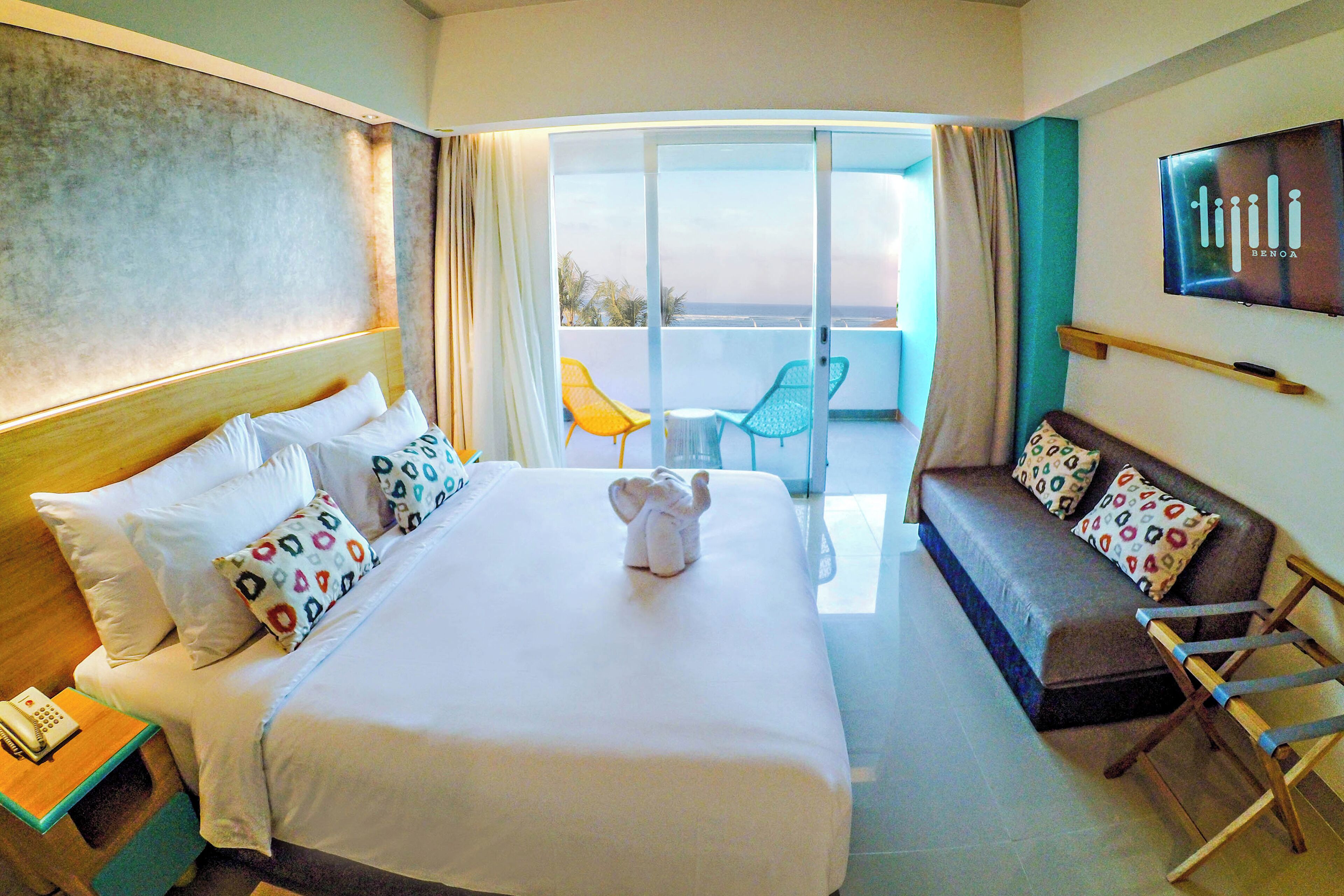 Habitación de hotel con cama, sofá, televisión y balcón con sillas.