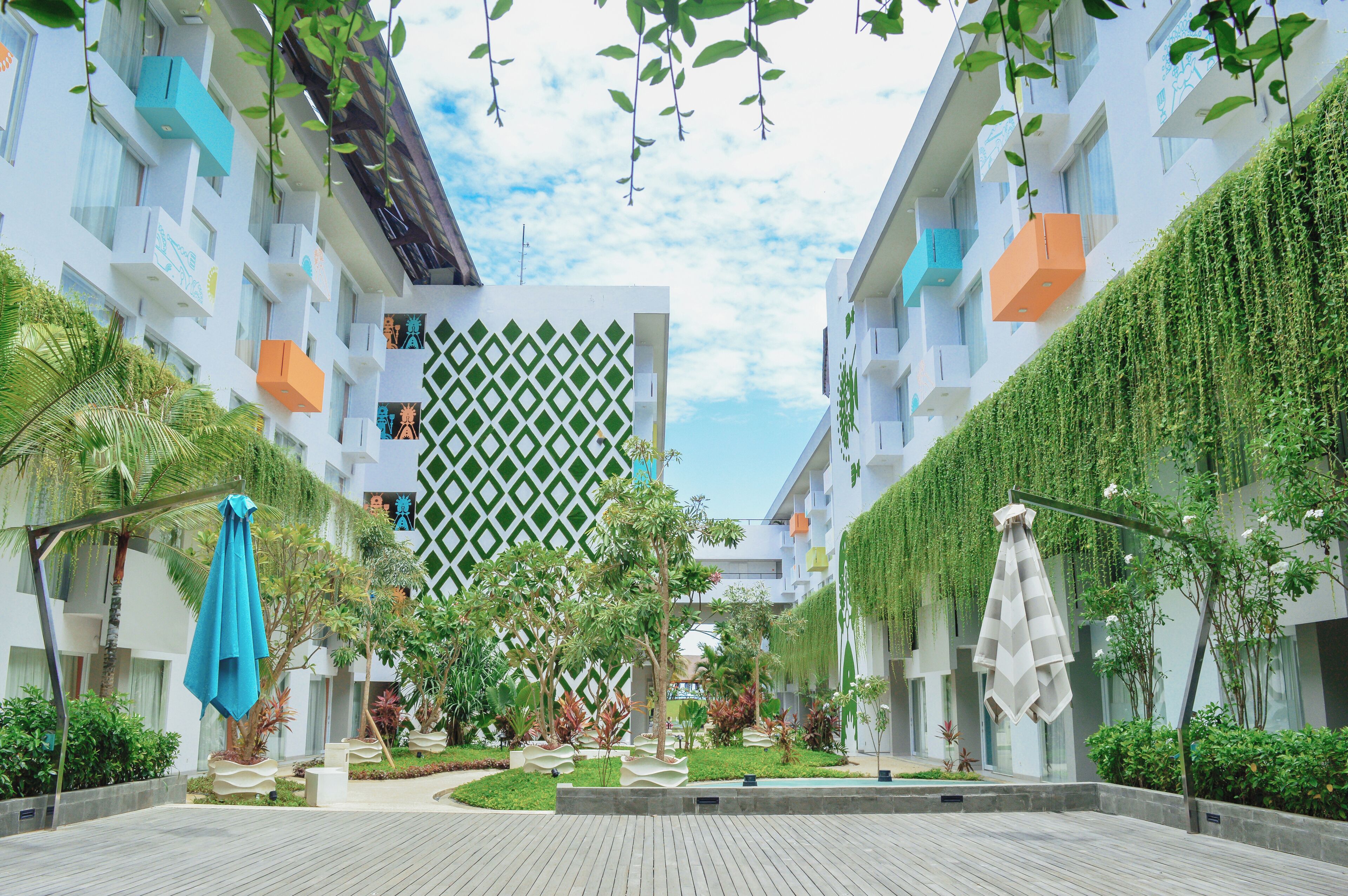 A modern building with balconies, a geometric wall pattern, and a garden area with trees and plants.