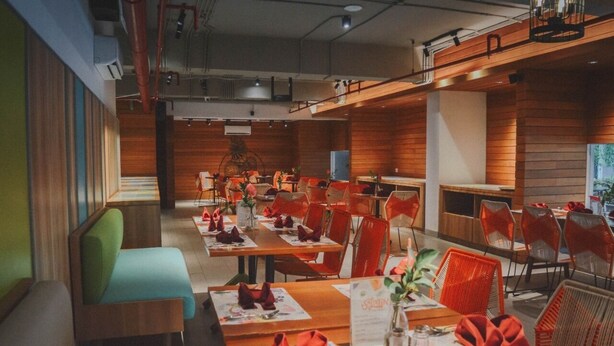 A restaurant with wooden panel walls, red chairs, and tables set with red napkins and menus. - Tijili Hotel Benoa (Nusa Dua)