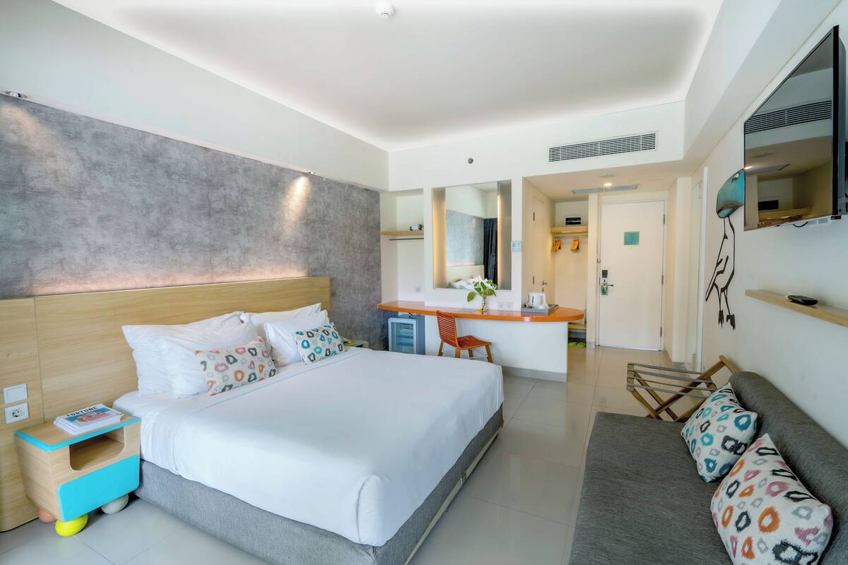 A modern hotel room with a large bed, a desk, and a seating area.