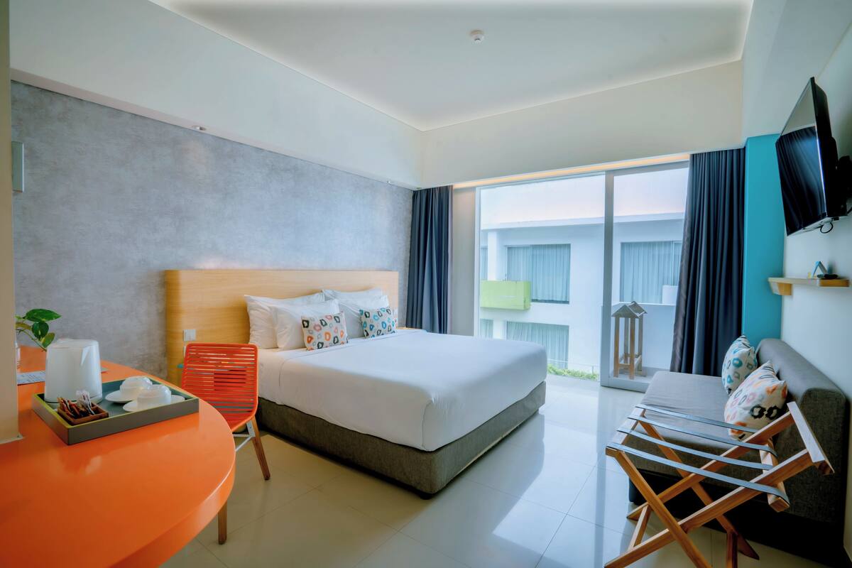 A modern hotel room with a large bed, a desk with a chair, a sofa, and a TV mounted on the wall.
