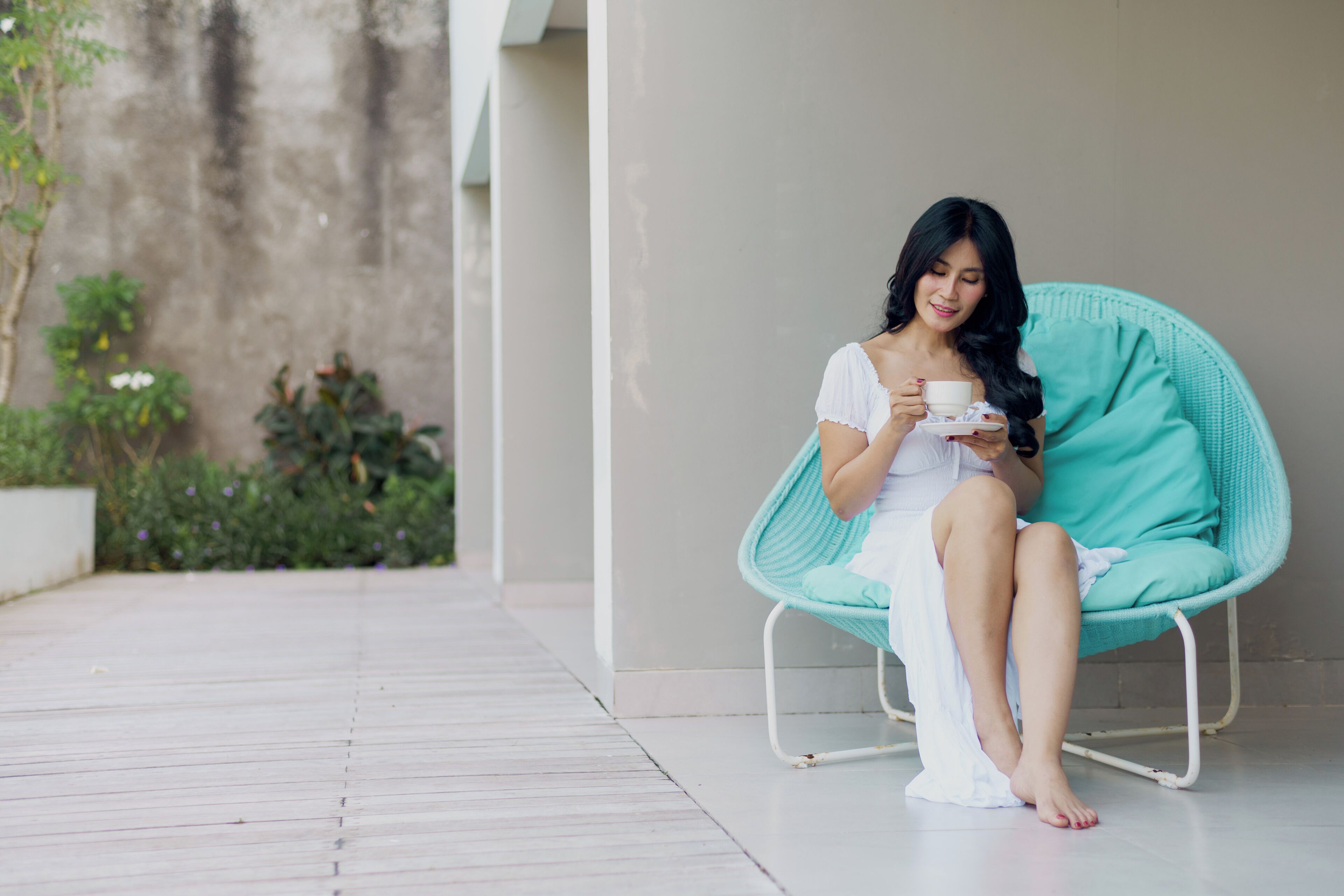 Une personne est assise sur une chaise de couleur turquoise dans une pièce dont un mur est en béton et où se trouvent des plantes en pot.