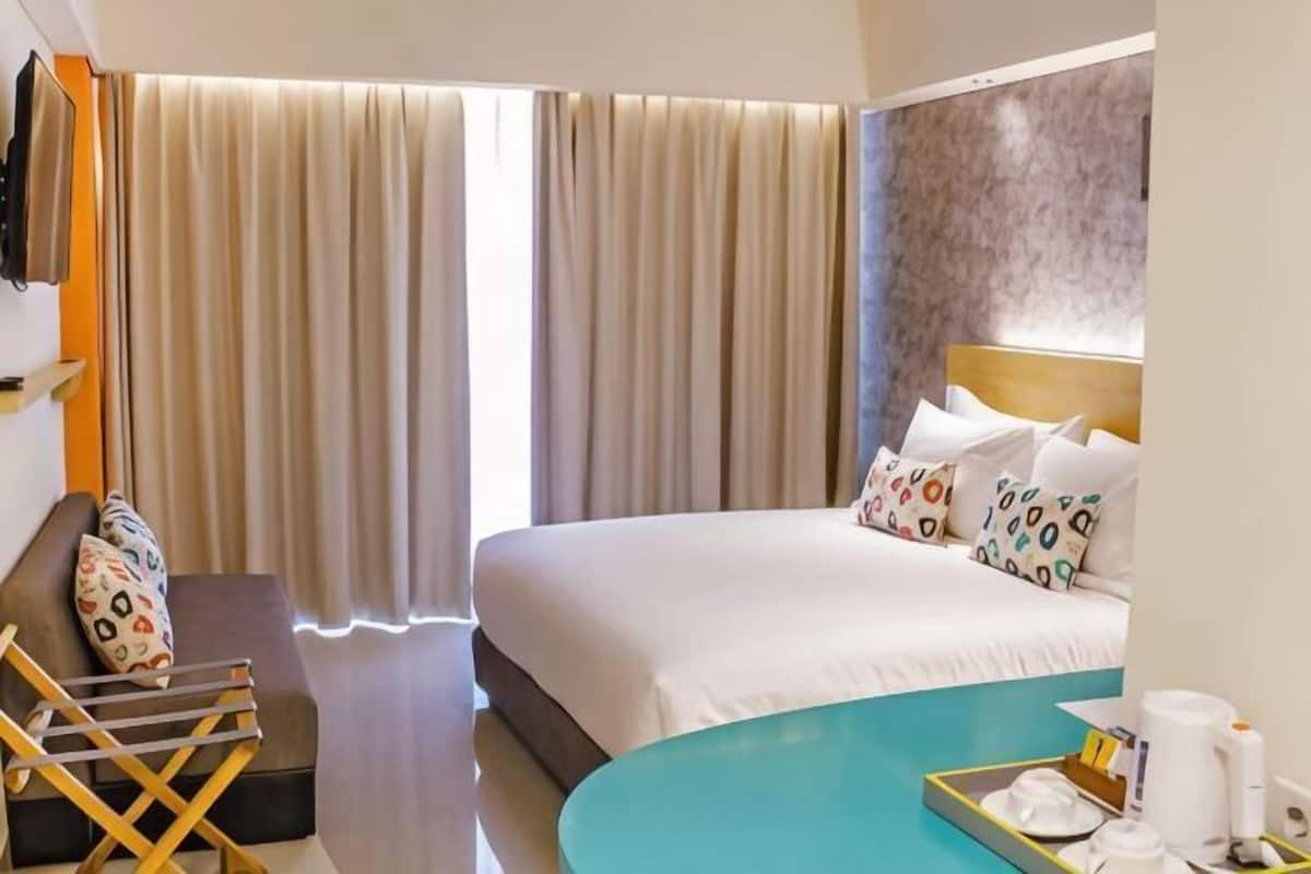 Ein Hotelzimmer mit einem Bett, einem Schreibtisch, einem Sessel, einem kleinen Tisch mit Tablett und einem Fenster mit Vorhängen.