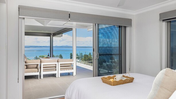 Quarto com uma grande porta de vidro deslizante que dá para uma varanda com vista para o mar.