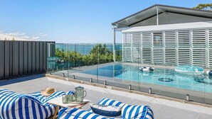 Área de piscina no terraço, com barreira de vidro, espreguiçadeiras e vista para o mar.