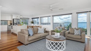 Uma sala de estar moderna com dois sofás, uma mesa de centro e janelas amplas com vista para o mar.