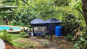 Un jardin avec une piscine, un kiosque et un réservoir d’eau bleu.