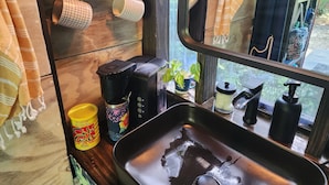 Un coin cuisine comprenant un évier, une machine à café, une plante et divers ustensiles de cuisine rangés sur des étagères.