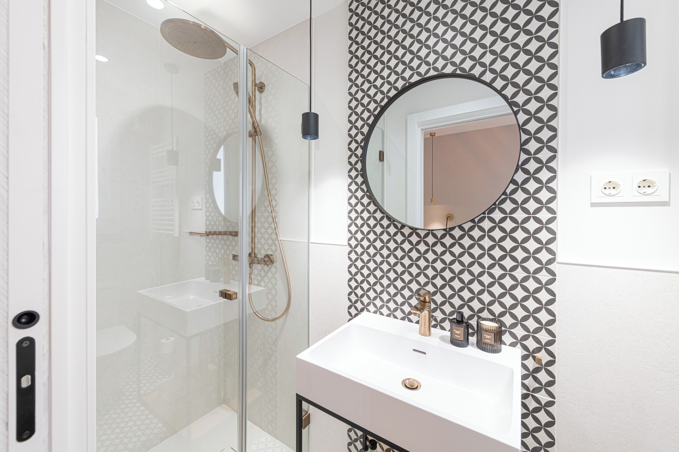 Een moderne badkamer met een douchecabine van glas, een witte wastafel met gouden details en een patroonbehang.