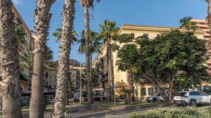 A street lined with palm trees and buildings, including a restaurant and a multi-story building with balconies. - Solaga - Gutenberg Beach (Málaga)
