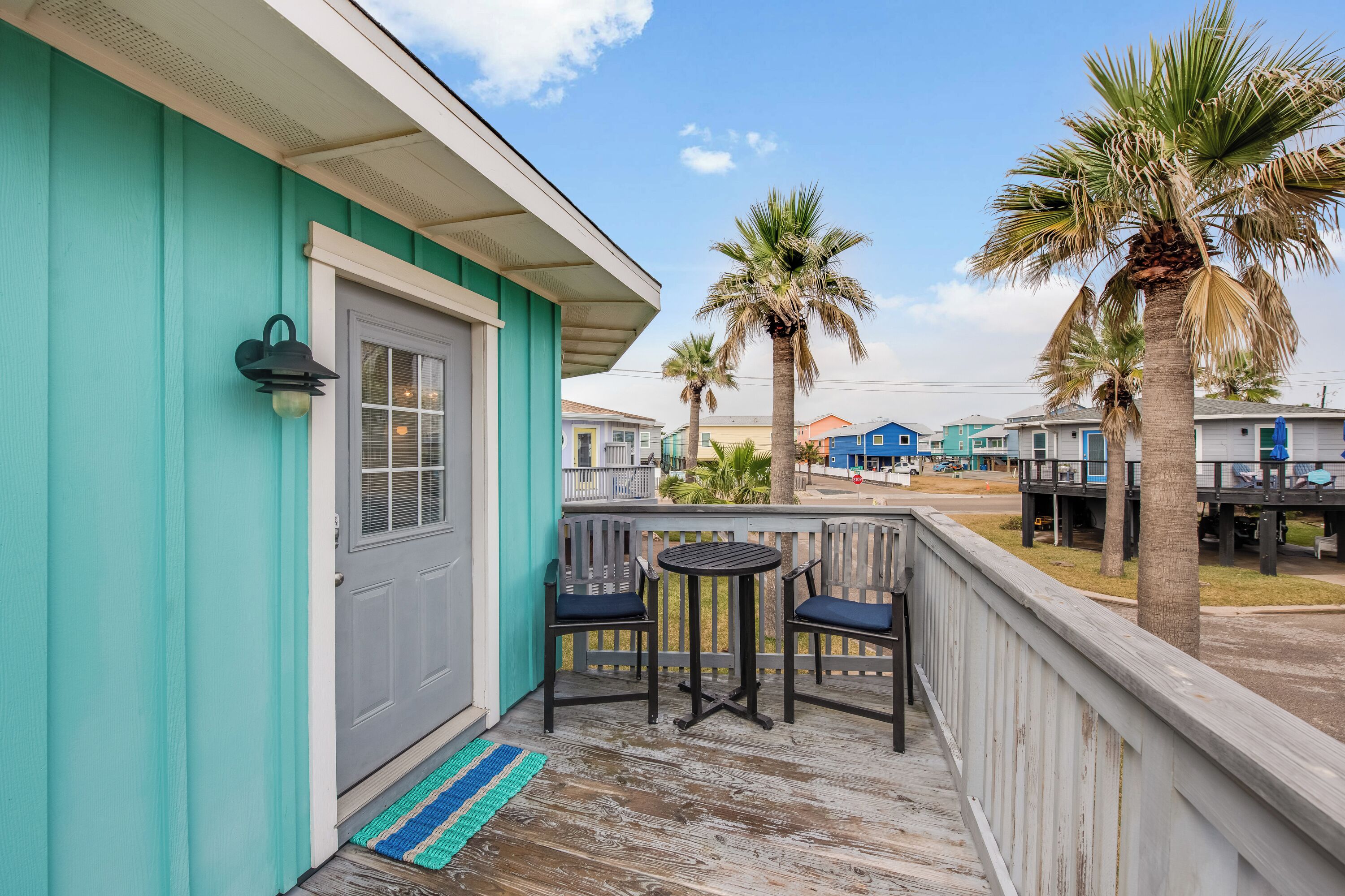 A turquoise building with a wooden deck, two chairs, and a small table.