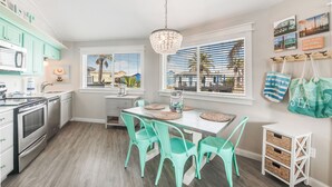 A modern kitchen with teal cabinets, a dining table with chairs, and a view of palm trees through large windows. - Adorable Port Aransas beach cottage with community pool and outdoor spaces.  Clo (Port Aransas)
