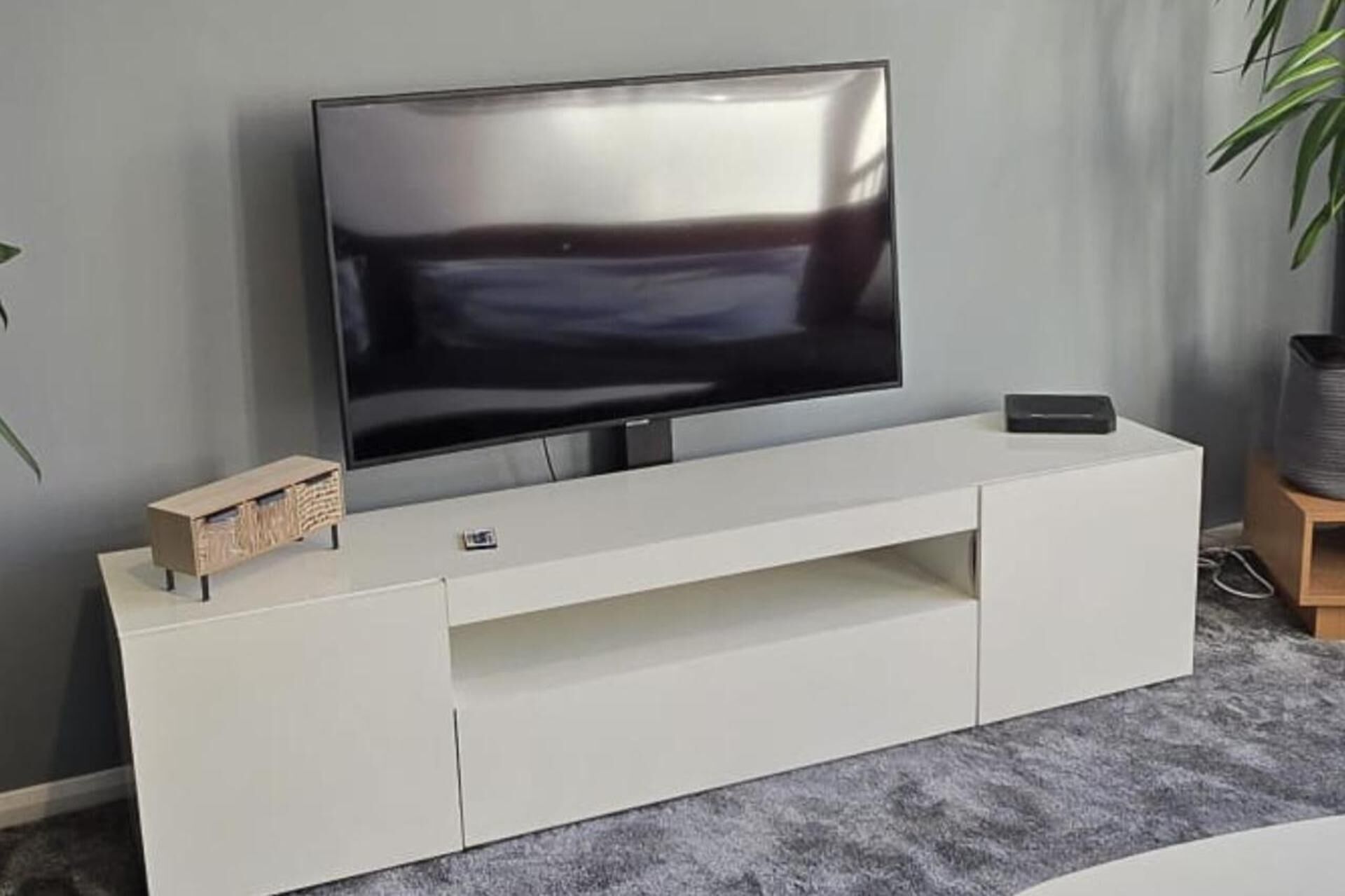 A flat-screen TV on a white entertainment unit with a shelf below.