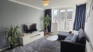 Ein Wohnzimmer mit Fernseher, Sofa und Topfpflanzen.