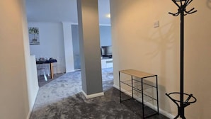 Ein Flur mit grauem Teppich, einem kleinen, schwarzen Metalltisch und einer hohen, schwarzen Stehlampe.
