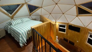 Una habitación con un diseño geométrico en el techo, una cama con ropa de cama a rayas, una mesa de madera y una ventana pequeña.