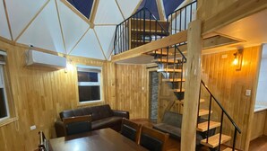 Un comedor amplio con una gran mesa de madera y sillas, una chimenea empotrada y una escalera de madera que sube a un nivel superior.