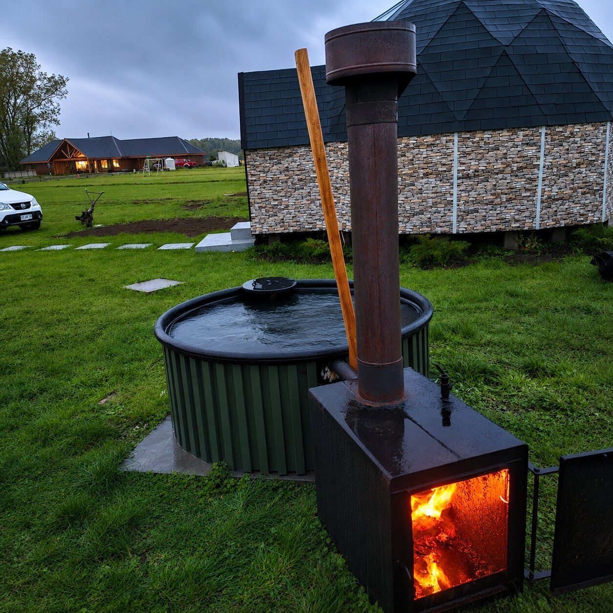 Una estufa de leña con chimenea, un calentador exterior verde y una pared de piedra al fondo.