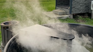 Un jacuzzi con vapor, un edificio de piedra y un campo de césped al fondo.