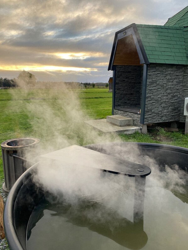 Un jacuzzi con vapor, un edificio de piedra y un campo de césped al fondo.