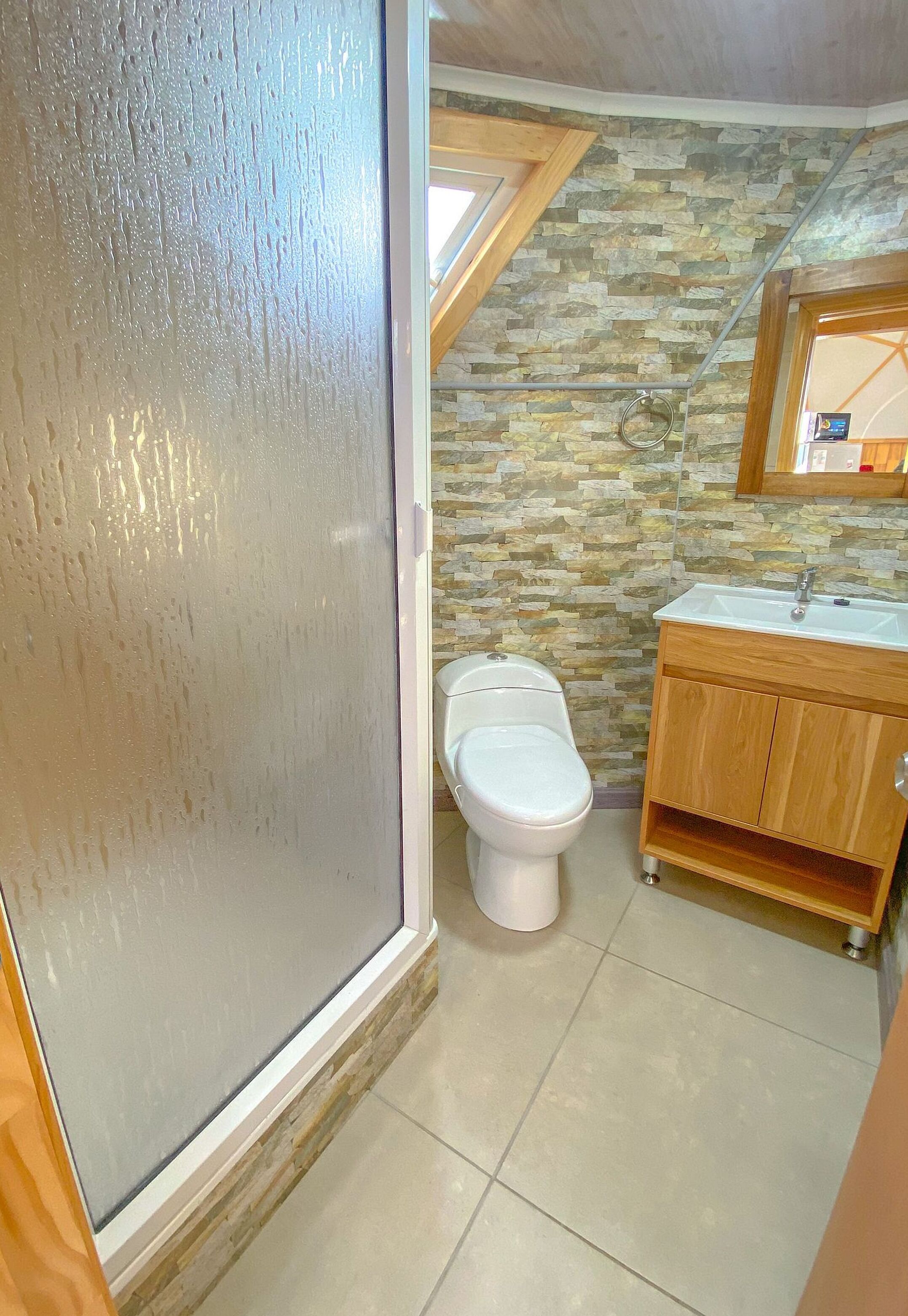 Un baño con pared de piedra, inodoro, gabinete de madera y espejo.