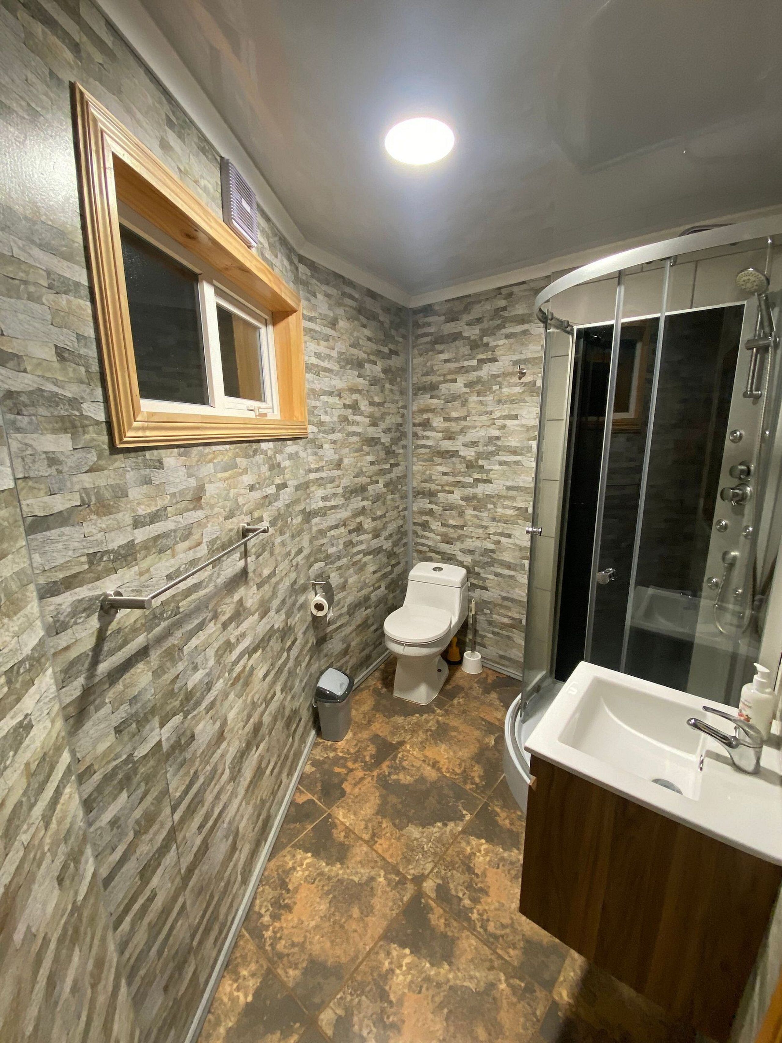 Un baño con pared de piedra, inodoro, ducha y lavamanos.