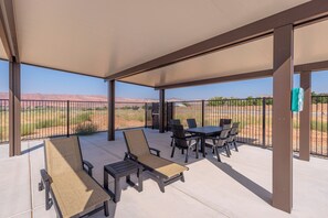 A covered patio with lounge chairs and a table, offering a view of a baseball field and mountains.