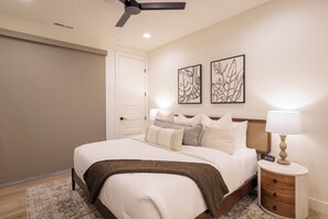 A bedroom with a bed, bedside table, lamp, and artwork on the wall.