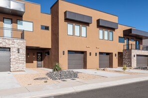 A modern multi-story residential building with a stone facade, multiple garage doors, and a landscaped front yard.
