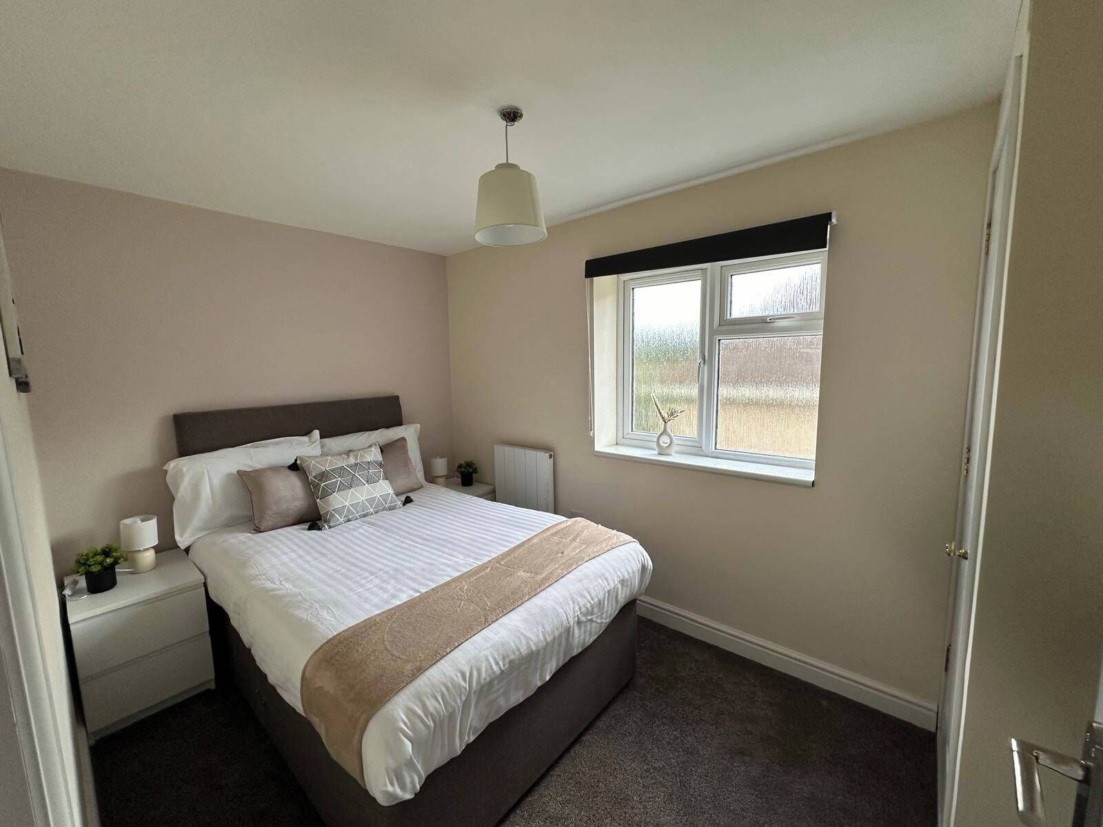 Een slaapkamer met een bed, nachtkastjes, een raam en een plafondlamp.