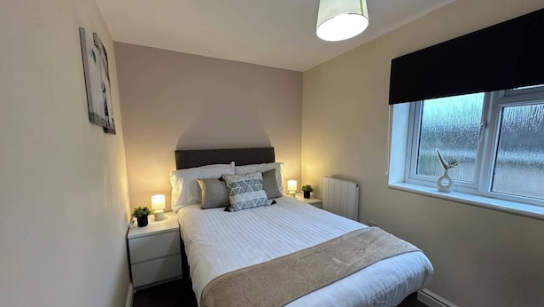 Ein ordentlich eingerichtetes Schlafzimmer mit Bett, Nachttischlampen, einem Fenster und einer Wandleuchte.