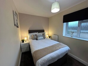 A neatly arranged bedroom with a bed, bedside lamps, a window, and a wall-mounted light fixture.