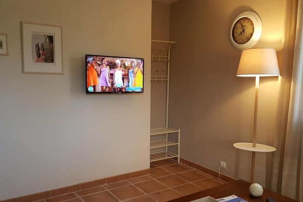 Ein Zimmer mit an der Wand befestigtem Fernseher, einer Stehlampe und einem Regal.
