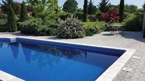 A rectangular swimming pool with a tiled edge, surrounded by a paved patio area.