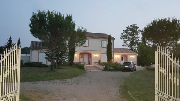 A two-story house with a driveway leading to the entrance, surrounded by trees and a car parked outside.